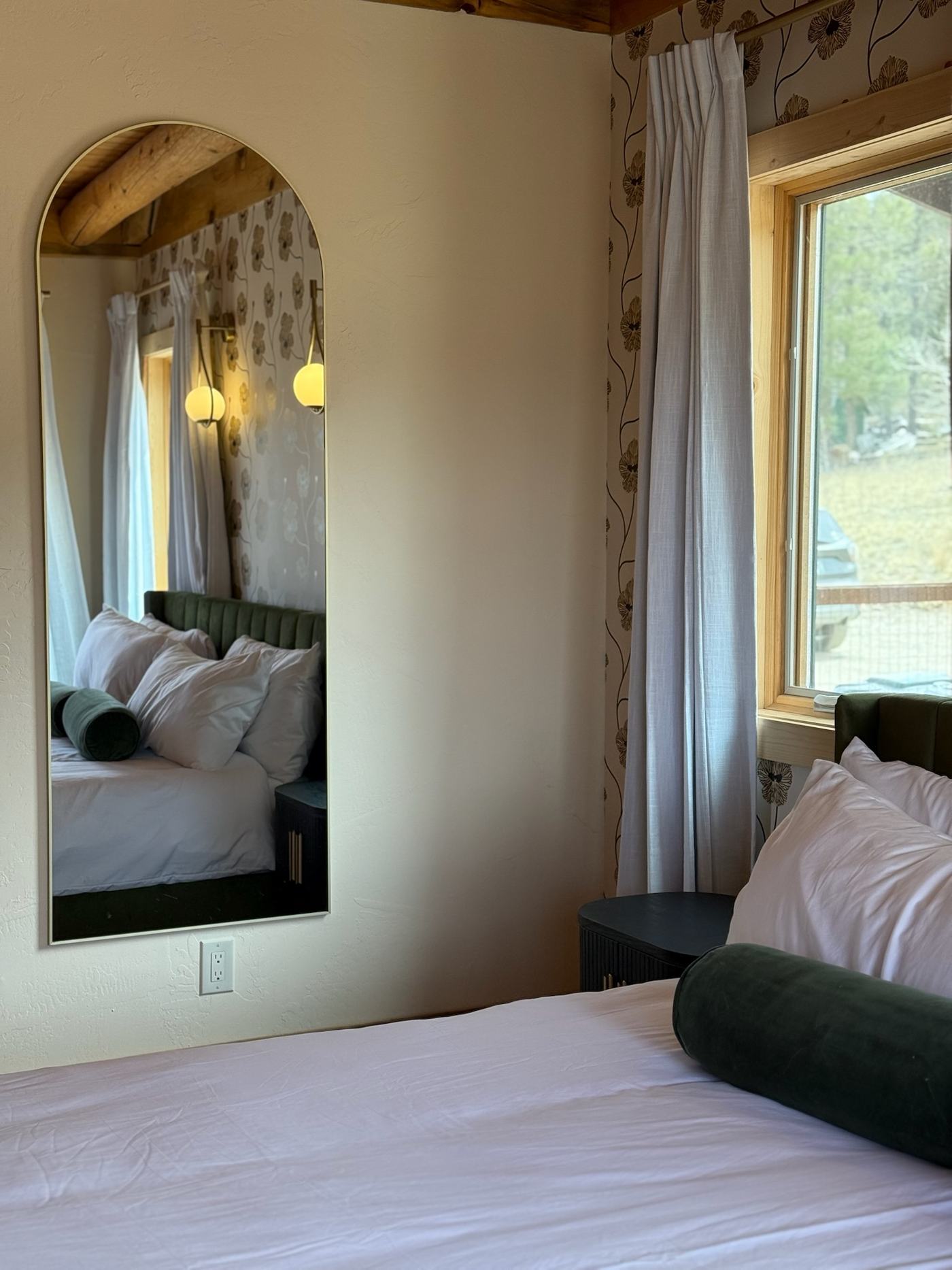 King bedroom with green channel-tufted bed and arched mirror