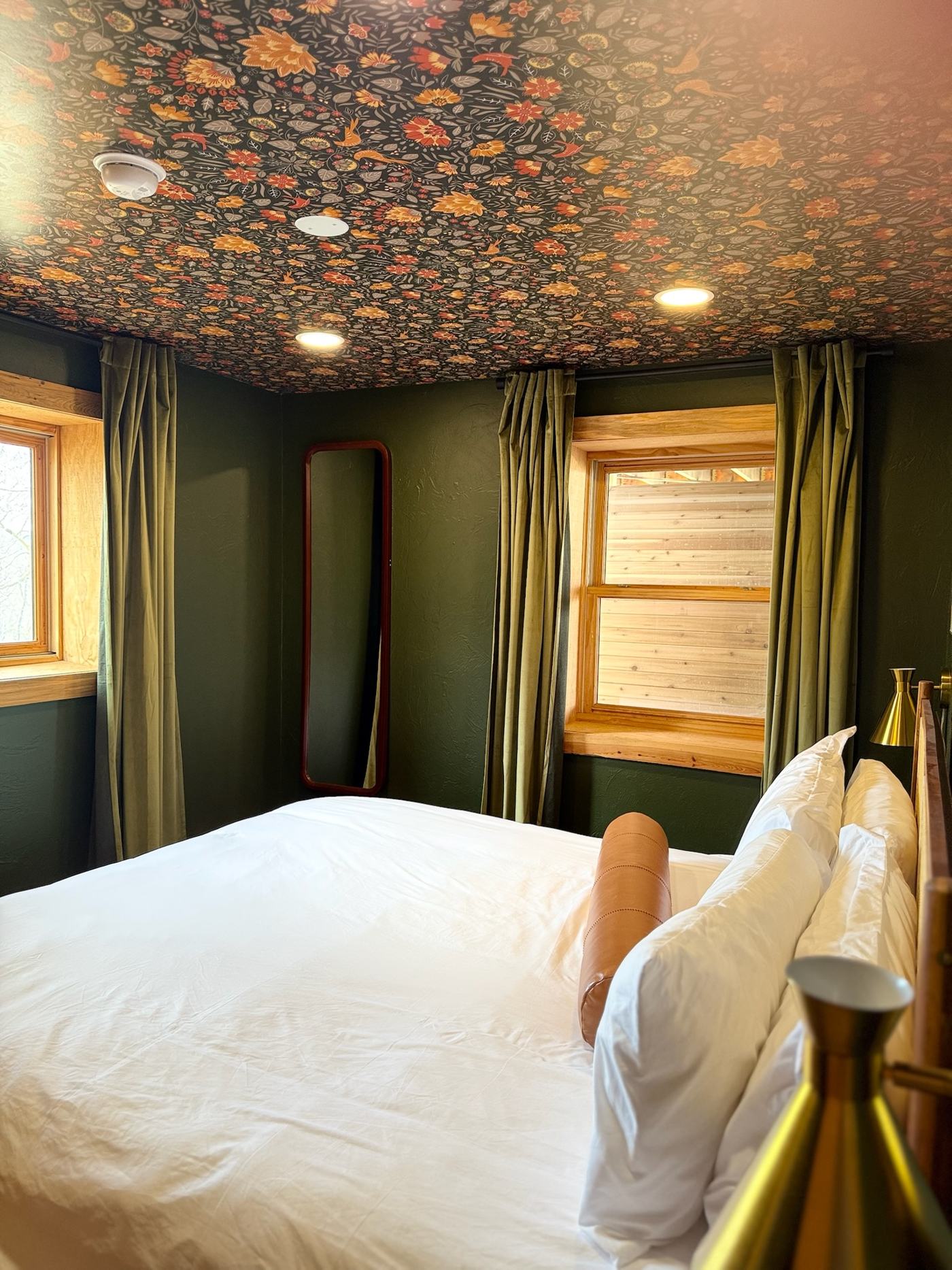 Green bedroom with floral wallpapered ceiling and brass sconces
